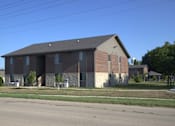Thumbnail 2 of 13 - A large brick building with a grey roof and a small porch.