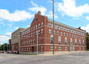 Thumbnail 1 of 17 - A large red brick building with a parking lot in front.