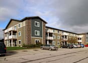 Thumbnail 1 of 12 - Apartment building with cars parked in front.