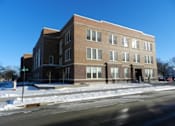 Thumbnail 1 of 11 - A large brick building with a snow-covered ground in front.