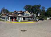 Thumbnail 1 of 7 - A building with a grey roof and a red door is surrounded by a parking lot.