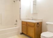Thumbnail 18 of 19 - A white bathroom with a wooden cabinet and a white toilet.