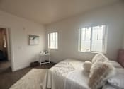 Thumbnail 7 of 14 - A white bedroom with a bed, a small table, and a window.