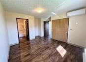 Thumbnail 12 of 21 - an empty living room with wood flooring and a door to a bathroom