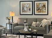 Thumbnail 17 of 21 - A living room with a grey couch, a coffee table, and two framed pictures on the wall.