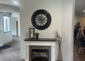 Thumbnail 19 of 21 - A clock hangs on a wall above a fireplace in a room.