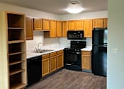 Thumbnail 5 of 12 - A kitchen with wooden drawers and a black fridge.