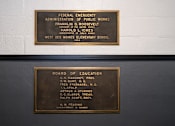 Thumbnail 18 of 22 - Two plaques on a wall, one above the other, listing the names of various administrators and board members.