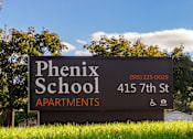 Thumbnail 19 of 22 - A sign for Phoenix School Apartments is displayed in front of a tree.