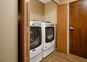 Thumbnail 14 of 14 - A laundry room with two washing machines and a wooden door.