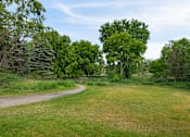 Thumbnail 24 of 25 - a grassy area with a gravel path and trees in the background  at Shadow Hills, Plymouth, MN, 55442