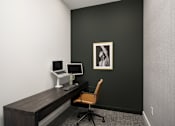 Thumbnail 16 of 22 - A black wall with a framed picture and a desk with a laptop and a monitor.