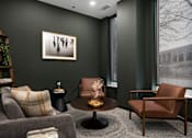 Thumbnail 17 of 22 - A living room with a grey couch, a brown chair, and a coffee table.