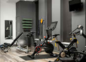 Thumbnail 12 of 22 - A gym with a variety of exercise equipment including a stationary bike, a rowing machine, and a weight bench.