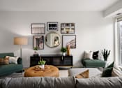 Thumbnail 5 of 22 - A living room with a grey sofa, a green chair, a wooden coffee table, and a mirror on the wall.