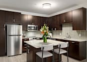 Thumbnail 1 of 22 - A modern kitchen with a stainless steel refrigerator, microwave, and white countertops.