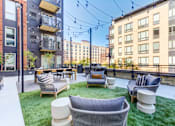 Thumbnail 19 of 22 - A patio with a white couch and chairs with a black railing and a building in the background.