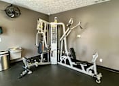 Thumbnail 14 of 19 - A home gym with a weight machine, a bench, and a fan.