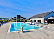 Thumbnail 56 of 57 - A large outdoor swimming pool with lounge chairs and a building in the background.