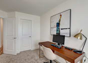 Thumbnail 9 of 20 - A room with a desk and a chair with a painting hanging on the wall.