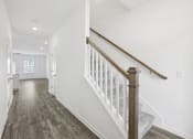 Thumbnail 12 of 27 - A long hallway with a staircase and wood flooring.