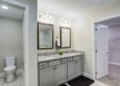 Thumbnail 9 of 19 - A bathroom with a toilet, two sinks, and a mirror.