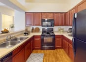 Thumbnail 27 of 30 - A kitchen with a black refrigerator, wooden cabinets, and a black stove top oven.