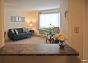 Thumbnail 38 of 43 - A living room with a dark green couch, a coffee table with a vase of flowers, and a window with white curtains.