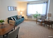 Thumbnail 37 of 43 - A living room with a blue couch, a grey armchair, a wooden table, and a carpet.