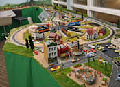 Thumbnail 49 of 49 - A model of a town with buildings, roads, and vehicles is displayed on a table.