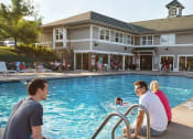 Thumbnail 3 of 28 - a group of people sitting at a pool with a building in the background