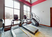 Thumbnail 27 of 64 - A treadmill and a stationary bike are in a gym with a view of the outside.