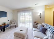 Thumbnail 61 of 65 - A living room with a grey couch, a coffee table, a flat screen TV, and a window with blinds.