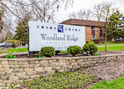 Thumbnail 124 of 124 - A sign for Woodland Ridge Apartments stands in front of a brick building.