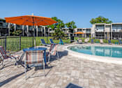 Thumbnail 36 of 53 - A pool area with a table and chairs and an orange umbrella.