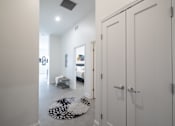Thumbnail 18 of 27 - A hallway with a rug and a bedroom with a bed and a dresser.