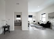 Thumbnail 17 of 27 - A living room with a black couch and a small table with a vase of flowers on it.