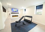 Thumbnail 25 of 27 - A black and white exercise machine in a room with a fireplace and a television.