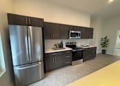 Thumbnail 3 of 27 - A modern kitchen with a stainless steel refrigerator and dark brown cabinets.