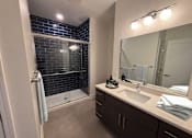 Thumbnail 11 of 27 - A bathroom with a white sink and a shower with a glass door.