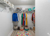 Thumbnail 11 of 35 - A white closet with clothes hanging and baskets underneath.