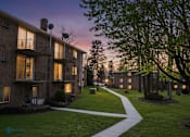 Thumbnail 1 of 17 - Apartment complex with a walkway and trees.