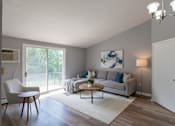 Thumbnail 12 of 17 - A living room with a white chair, a grey couch, a coffee table, and a painting on the wall.