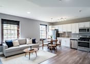 Thumbnail 8 of 29 - A modern kitchen with a grey couch and wooden chairs.