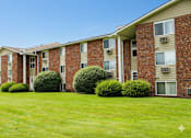 Thumbnail 52 of 67 - A row of red brick apartment buildings with green bushes in front.