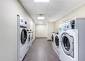 Thumbnail 18 of 29 - A row of industrial washing machines are lined up in a clean, empty room.