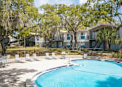 Thumbnail 29 of 47 - A swimming pool surrounded by trees and chairs in front of a building.