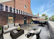 Thumbnail 21 of 29 - A patio with a table and chairs is set up outside a brick building.
