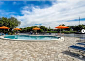 Thumbnail 27 of 47 - A round pool with a tiled floor and orange umbrellas in the background.