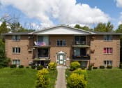 Thumbnail 13 of 15 - a brick apartment building with a green lawn and a flag on the balcony